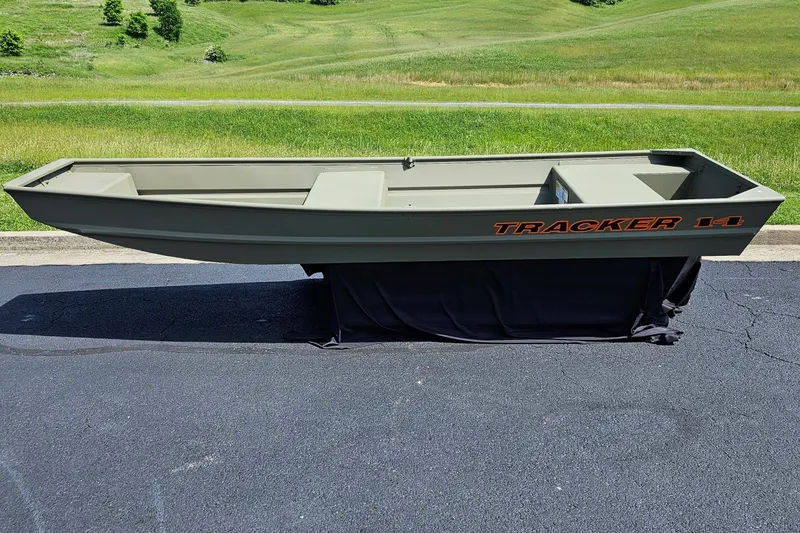 The Image of 2026 Tracker Grizzly 14 Jon boat on pavement, green landscape background. - 0