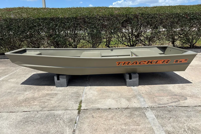 The Image of 2026 Tracker Grizzly 12 Jon boat on concrete blocks, outdoors, with hedge background. - 0