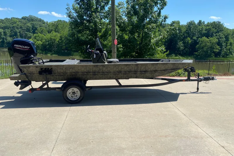 The Image of 2026 Tracker Grizzly 1860 CC boat on trailer, parked outdoors near a lake. - 0