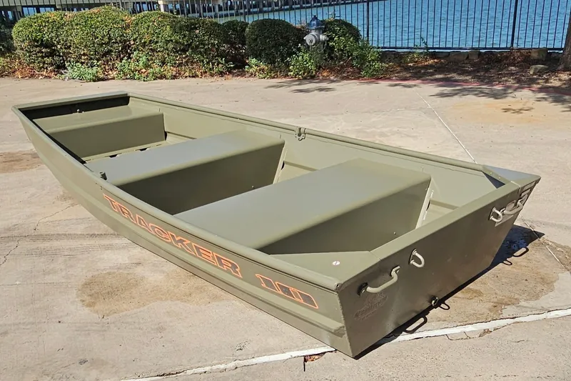 Slide: The Image of 2026 Tracker Grizzly 12 Jon boat on concrete near water, showcasing durable design. - 44