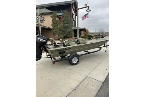 Slide: The Image of 2026 Tracker Grizzly 1754 SC boat on trailer, parked outdoors near a building and American flag. - 32