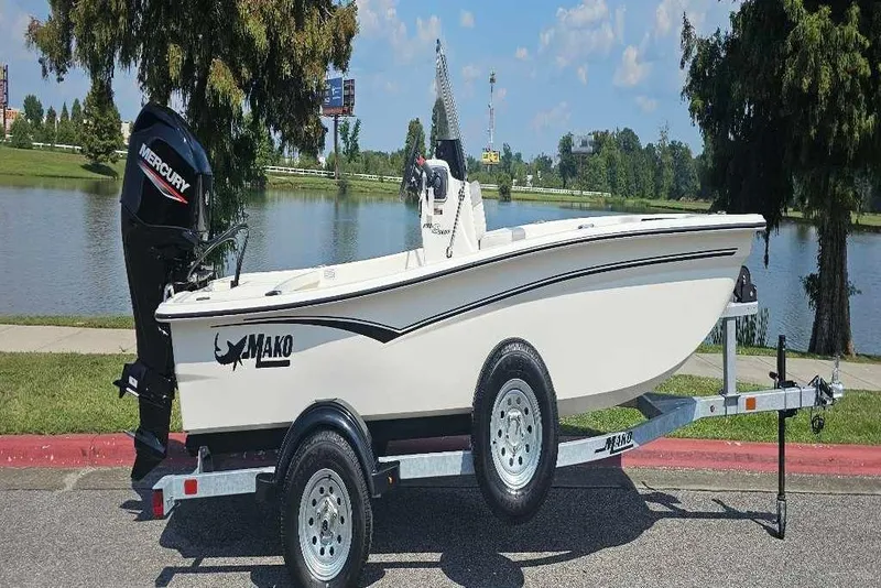 Slide: The Image of 2026 Mako Pro Skiff 15 CC boat on trailer by a scenic lake. - 1