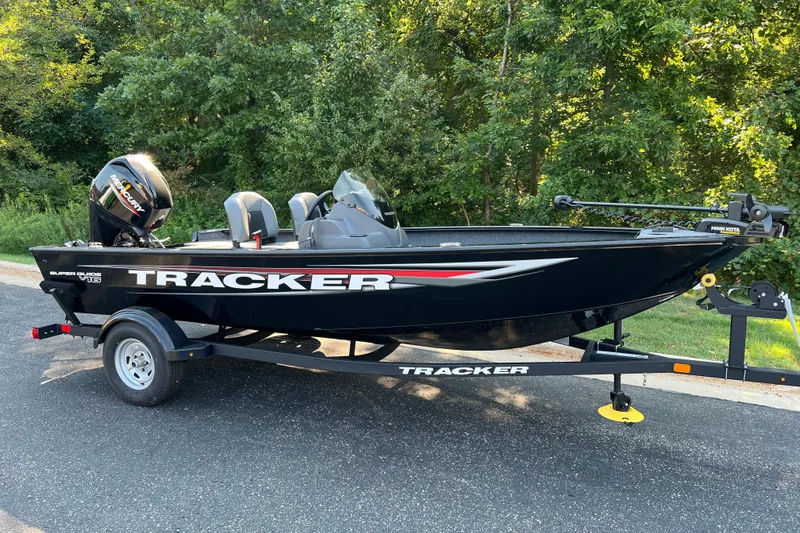 The Image of 2026 Tracker Super Guide V-16 SC boat on trailer, parked near lush greenery. - 0