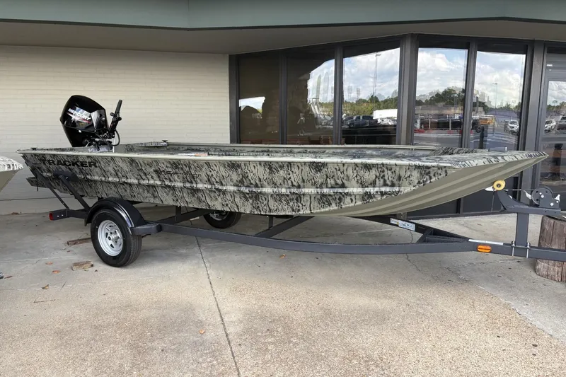 The Image of 2026 Tracker Grizzly 1654 T Sportsman boat on trailer, camo design, parked outside a building. - 0
