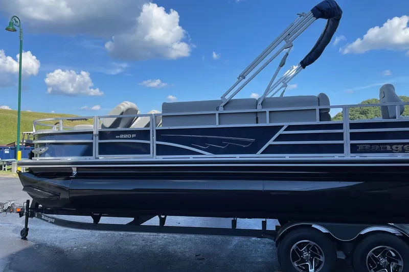 Slide: The Image of 2024 Ranger Reata 220F pontoon boat with canopy on trailer, set against a scenic backdrop. - 0