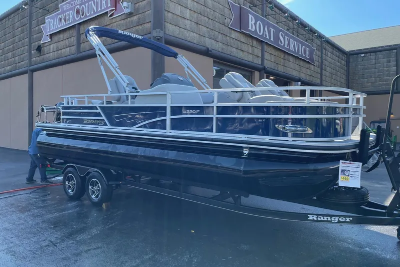 Slide: The Image of 2024 Ranger Reata 220F pontoon boat on trailer, blue with canopy, parked outdoors. - 1