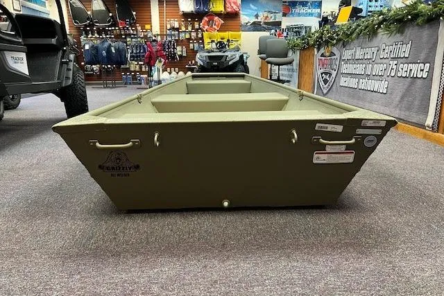 Slide: The Image of 2026 Tracker Grizzly 12 Jon boat displayed in a showroom with outdoor gear. - 7