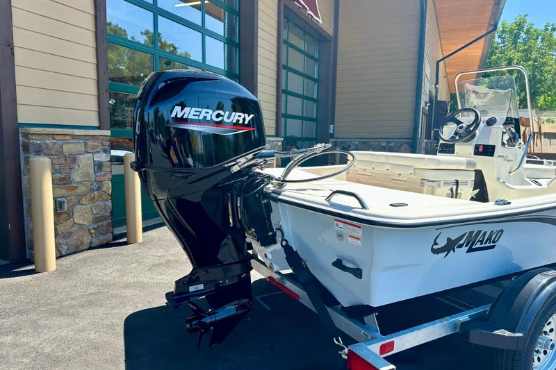 Slide: The Image of 2026 Mako Pro Skiff 15 CC boat with Mercury outboard motor, parked outside a building. - 2