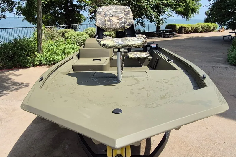 Slide: The Image of 2026 Tracker Grizzly 1754 SC boat with camouflage seating, parked near a scenic lakeside. - 2