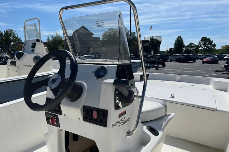 Slide: The Image of 2026 Mako Pro Skiff 17 CC boat console with steering wheel and controls in a parking lot. - 6