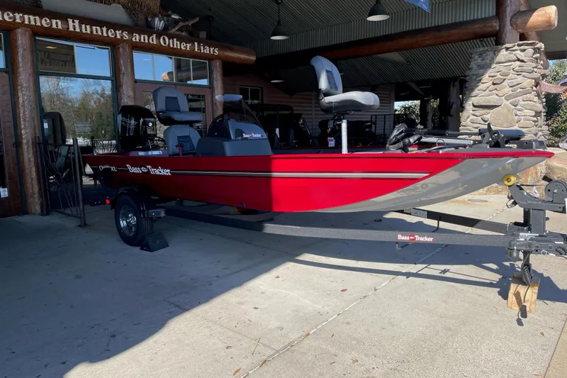 Slide: The Image of 2026 Tracker Bass Tracker Classic XL boat in vibrant red, parked outside a rustic building. - 2