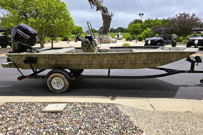 Slide: The Image of 2026 Tracker Grizzly 1860 CC boat on trailer, parked outdoors with trees in background. - 5