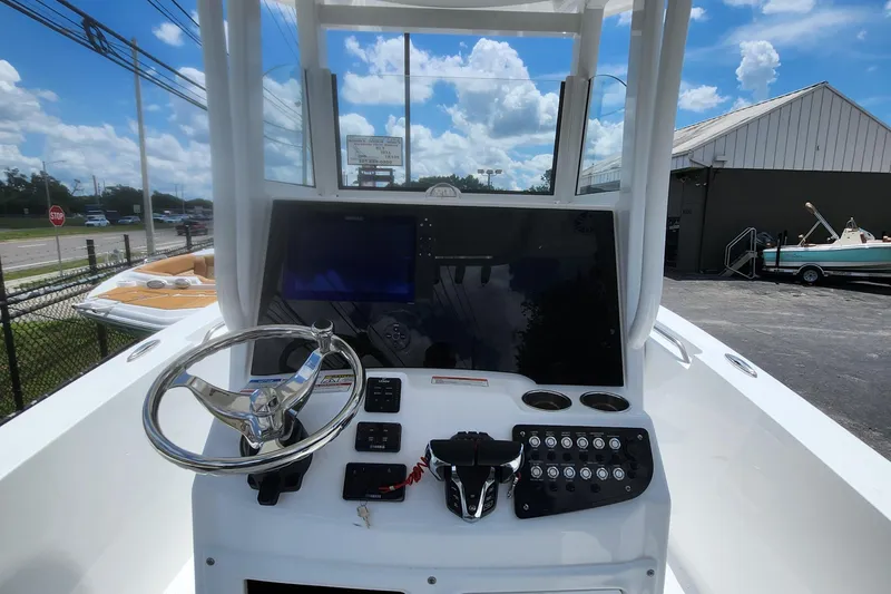 Slide: The Image of 2026 NauticStar 252 Legacy boat dashboard with steering wheel and control panel under blue sky. - 6