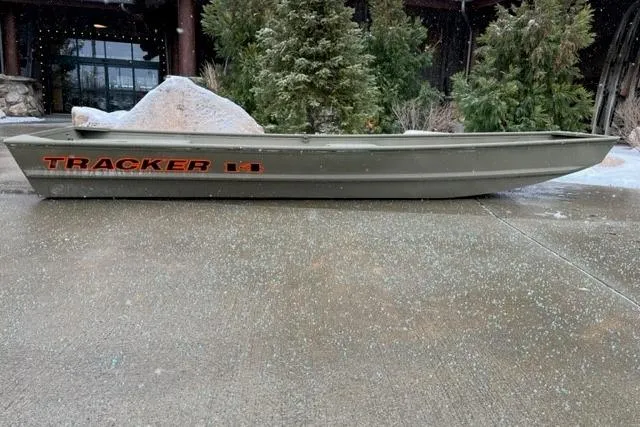 The Image of 2026 Tracker Grizzly 14 Jon boat on concrete, surrounded by trees. - 0