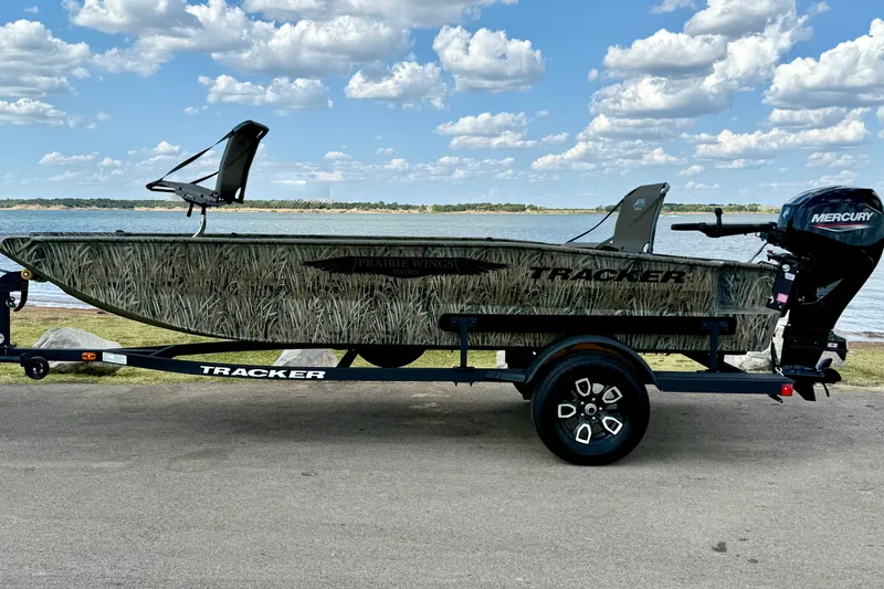 Slide: The Image of 2026 Tracker Grizzly 1650 T Prairie Wings Edition boat on trailer by a lake. - 14
