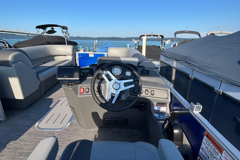 Slide: The Image of 2024 Bennington 22 SSR boat interior with steering wheel and seating, docked by the water. - 5