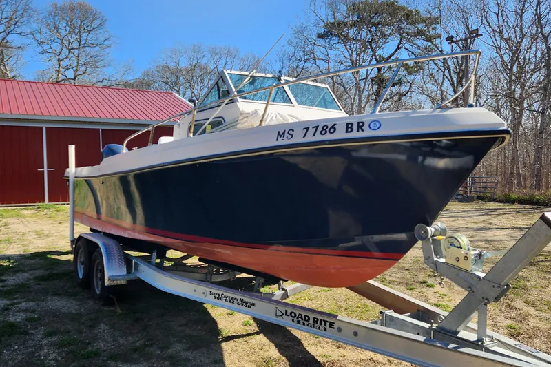 Slide: The Image of 1985 Sea Ox 23 boat on trailer, parked near red building, sunny day. - 2