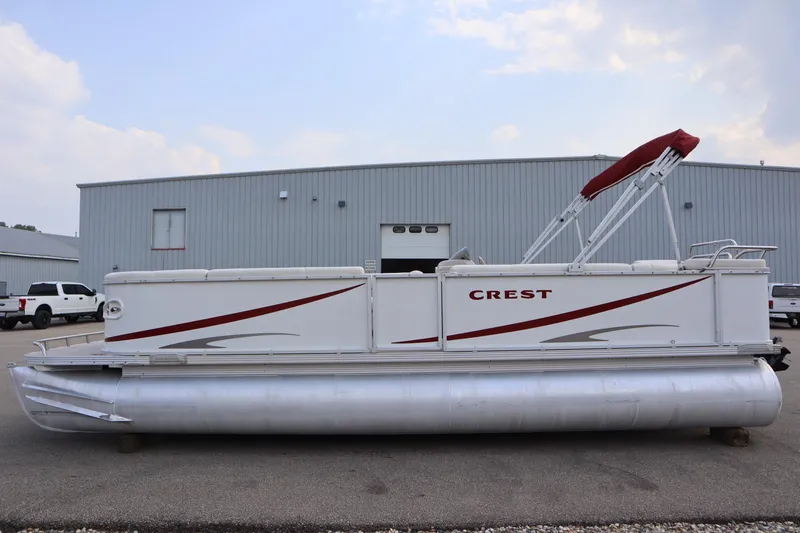Slide: The Image of 2005 Crest 25 Caribbean pontoon boat with red accents, parked near a warehouse. - 8