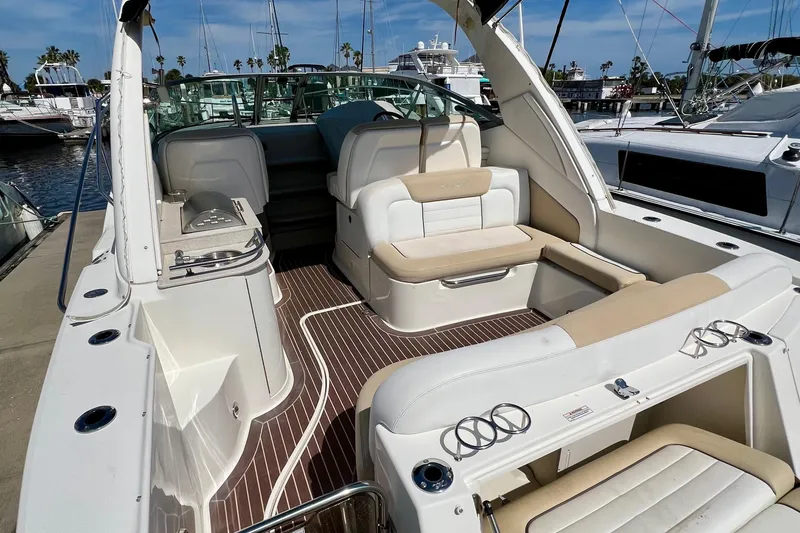 Slide: The Image of 2010 Sea Ray 350 Sundancer boat interior with white seating and wood flooring at a marina. - 10