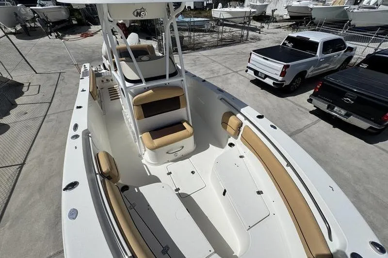 Slide: The Image of 2016 NauticStar 25 XS boat with tan seating, parked near trucks. - 14