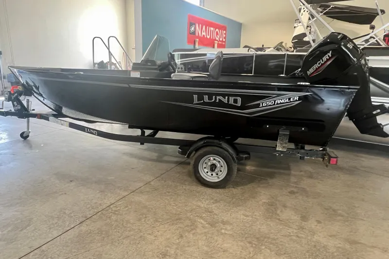 The Image of 2025 Lund 1650 Angler SS boat on trailer in showroom, featuring Mercury outboard motor. - 1