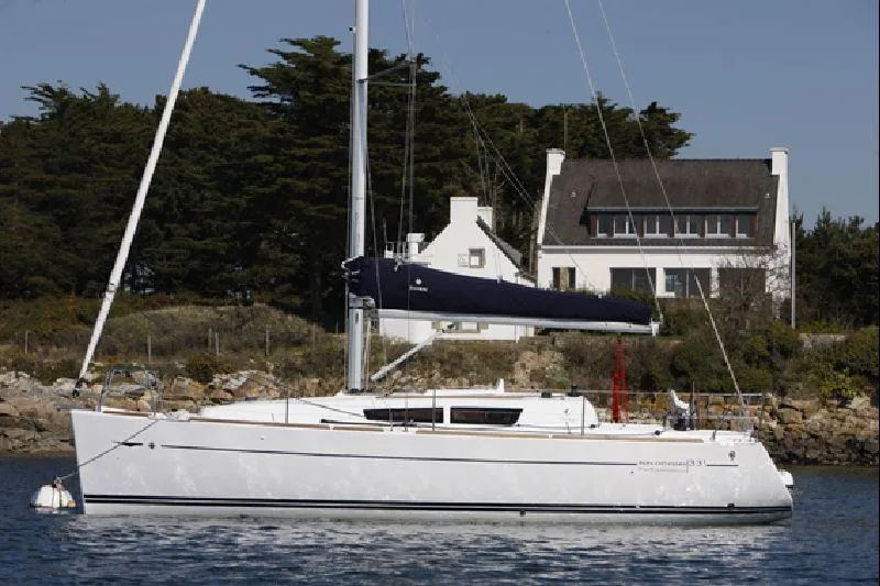 Slide: The Image of 2011 Jeanneau Sun Odyssey 33i sailboat on calm water near a coastal house. - 1