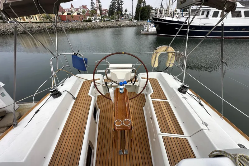 Slide: The Image of 2011 Jeanneau Sun Odyssey 33i sailboat cockpit with wooden deck and steering wheel, docked in marina. - 32