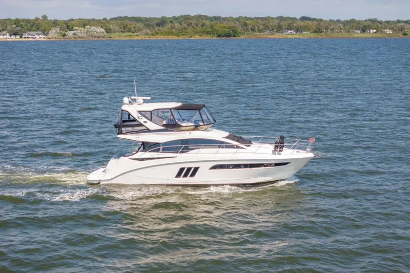 Slide: The Image of 2017 Sea Ray Fly 510 yacht cruising on a serene lake with lush green shoreline. - 4