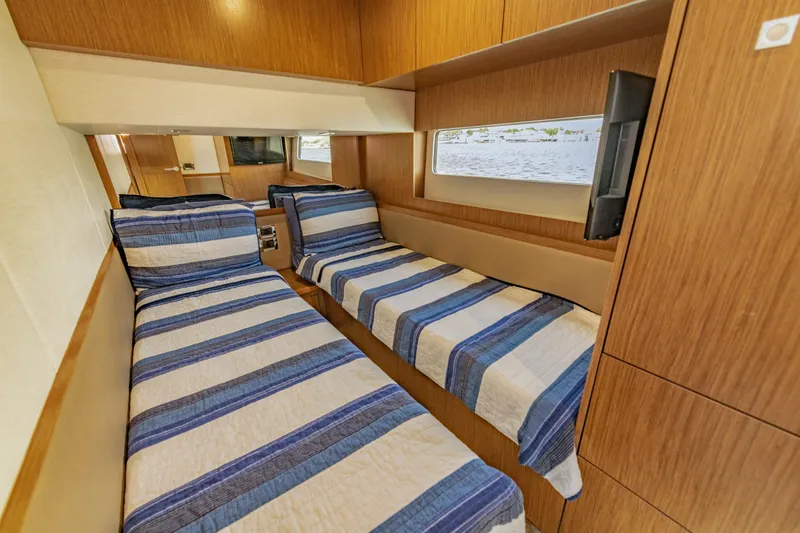 Slide: The Image of 2017 Sea Ray Fly 510 cabin with twin beds, striped bedding, and wooden interior. - 64