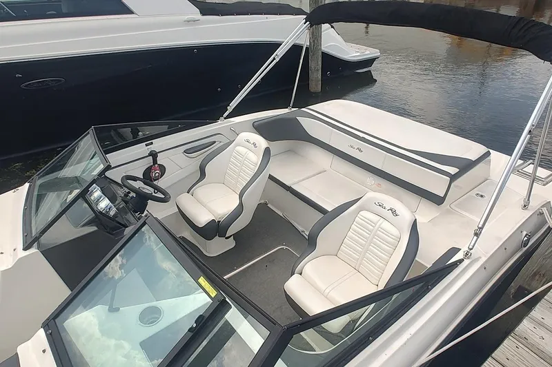 Slide: The Image of 2018 Sea Ray SPX 190 boat interior with white seating and steering wheel, docked by water. - 11