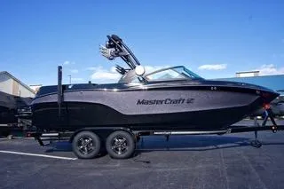 The Image of 2025 MasterCraft XT23 boat on trailer, sleek design, parked outdoors under clear blue sky. - 1