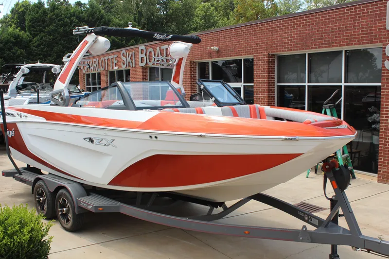 The Image of 2020 Tigé 23ZX boat in orange and white on a trailer outside a brick building. - 1