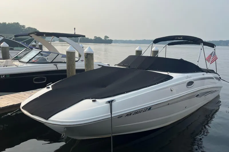 The Image of 2013 Sea Ray 280 Sundeck boat docked, covered, with American flag, on calm water. - 0