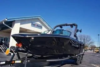 Slide: The Image of 2025 MasterCraft NXT23 boat on trailer outside dealership under clear blue sky. - 7