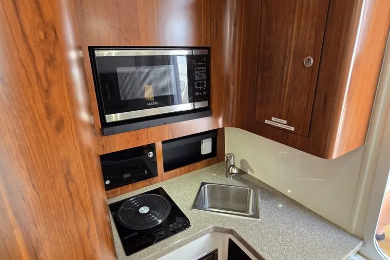 Slide: The Image of 2020 Regulator Motor Yacht kitchen with microwave, stove, and sink in wooden cabinetry. - 16