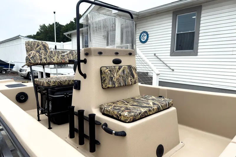Slide: The Image of 2026 Carolina Skiff E18 JVX CC Sportsman boat with camo seating, docked near a white building. - 28