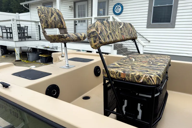 Slide: The Image of 2026 Carolina Skiff E18 JVX CC Sportsman boat with camo seating, docked near a white building. - 32