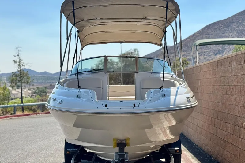 Slide: The Image of 2000 Sea Ray 240 Sundeck boat with canopy, parked near mountains and brick wall. - 2