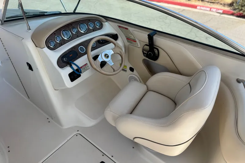 Slide: The Image of 2000 Sea Ray 240 Sundeck helm with steering wheel and gauges, featuring beige seating. - 25