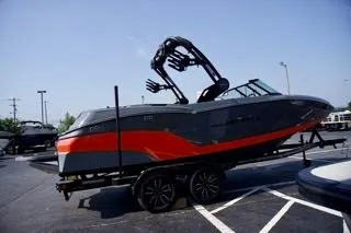 Slide: The Image of 2025 MasterCraft NXT22 boat with orange and gray design on a trailer in a parking lot. - 4