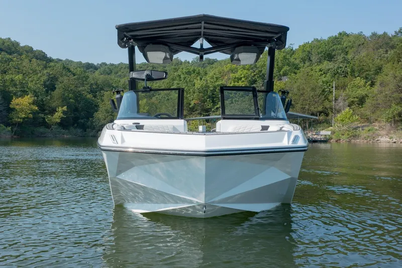 Slide: The Image of 2022 Nautique Super Air Nautique G25 boat on a serene lake with lush green background. - 2