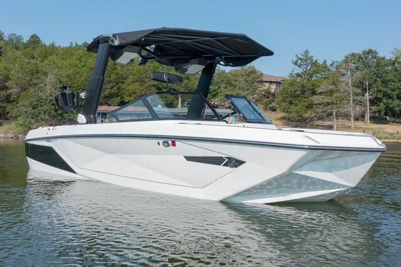 Slide: The Image of 2022 Nautique Super Air Nautique G25 boat on a calm lake, surrounded by trees. - 3