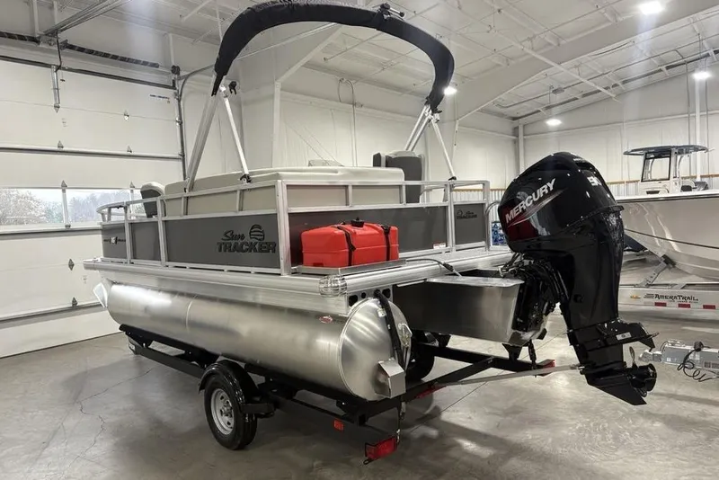 Slide: The Image of 2026 Sun Tracker Bass Buggy 16 XL Select pontoon boat with Mercury outboard motor in a garage. - 5