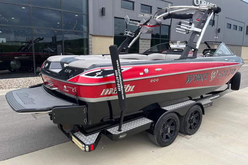 Slide: The Image of 2013 Malibu Wakesetter 23 LSV boat, red and black, on a trailer outside a building. - 2