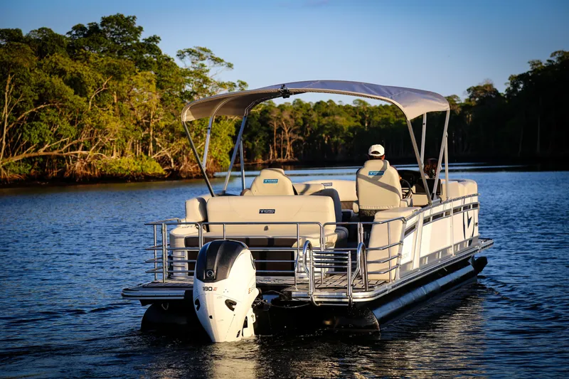 The Image of 2025 Vision Marine Technologies V24 pontoon boat cruising on a serene lake. - 1