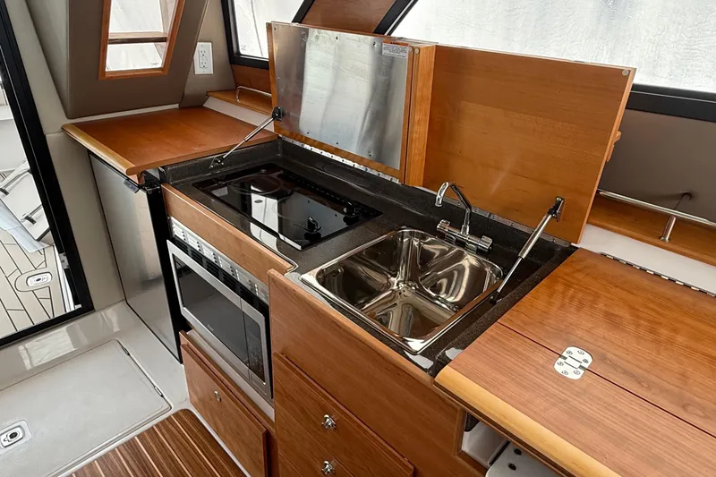 Slide: The Image of 2025 Cutwater C-32 CB yacht kitchen with stove, sink, and wooden cabinetry. - 23
