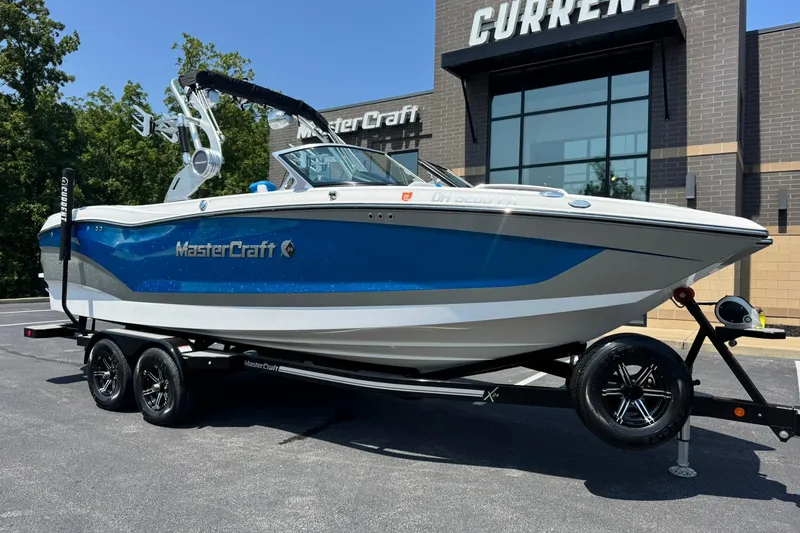The Image of 2020 MasterCraft X24 boat on trailer, parked outside dealership, featuring sleek blue and white design. - 1