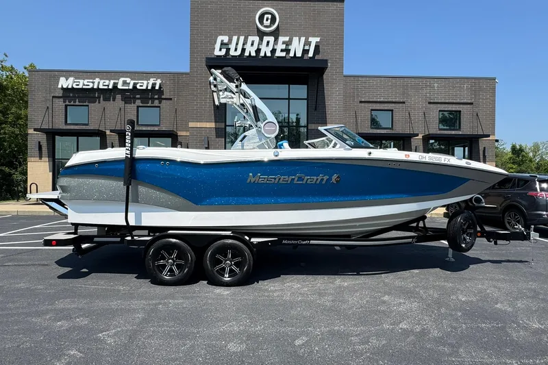 Slide: The Image of 2020 MasterCraft X24 boat on trailer outside dealership, featuring sleek blue and white design. - 20