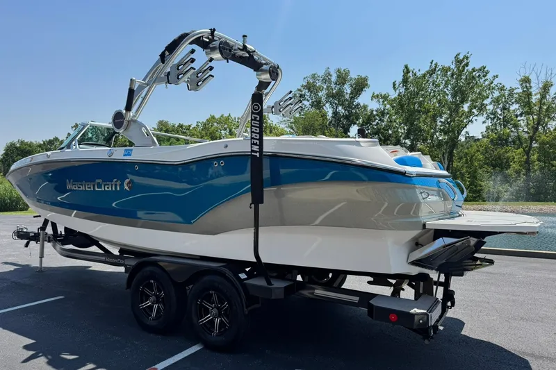 Slide: The Image of 2020 MasterCraft X24 boat on trailer, blue and white design, parked outdoors. - 5