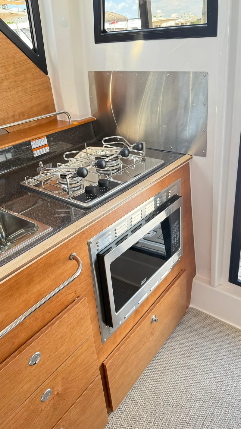 Slide: The Image of 2026 Cutwater C-288 Coupe interior kitchen with stove, microwave, and wooden cabinetry. - 31